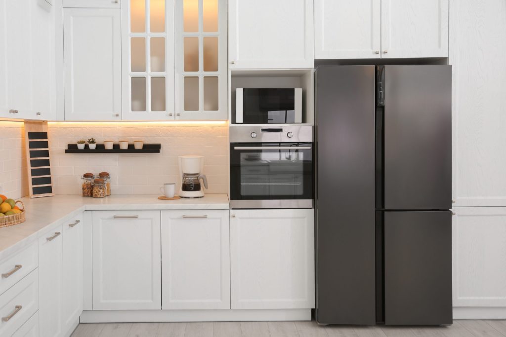A white shaker kitchen with a four-door refrigerator, a built-in wall oven and a microwave above it